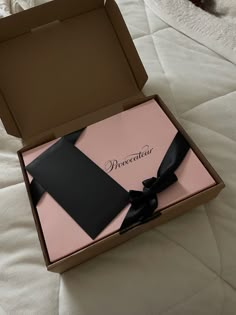 an open box with a black bow on it sitting on top of a white bed