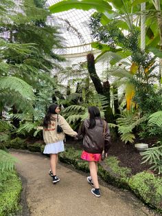 two girls walking down a path in a tropical garden with palm trees and other plants