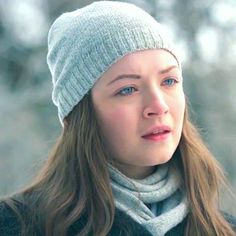 a woman with long hair wearing a gray hat and scarf, looking off to the side