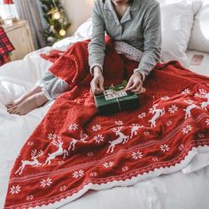 a woman sitting on top of a bed holding a green present under a red blanket