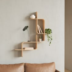 a brown couch sitting next to a wall mounted shelf filled with books and plant pots