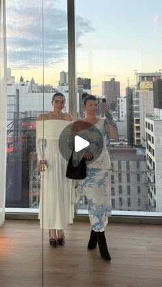 two women standing in front of a large window with cityscape and skyscrapers behind them