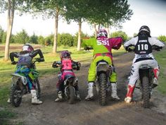 four people on dirt bikes in the middle of a road with trees and grass behind them