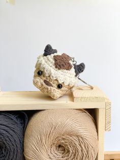 two balls of yarn and a crocheted cow head on top of a wooden shelf