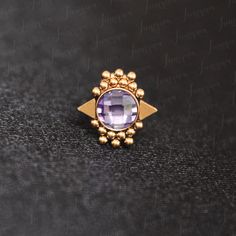 a gold ring with a purple stone in the center on a black surface, surrounded by beads