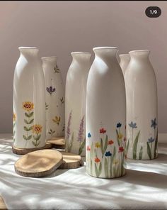 five vases with flowers painted on them sitting on a white table cloth next to slices of wood