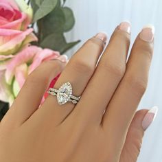 a woman's hand with a diamond ring on it and flowers in the background