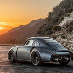 an old car parked on the side of a mountain road at sunset with mountains in the background