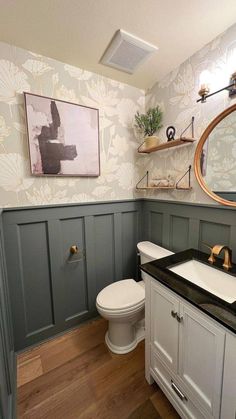 a white toilet sitting next to a sink in a bathroom under a framed painting on the wall