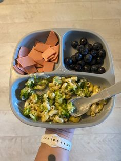 a person holding a tray with different types of food in it, including olives and broccoli