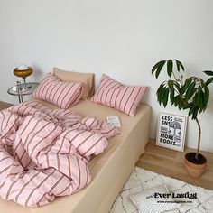 there is a bed with pink and white striped sheets on it, next to a potted plant