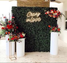 two tall white vases with flowers in front of a wall that says crazy inside