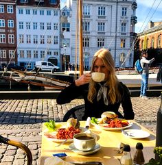 a woman sitting at an outdoor table drinking coffee