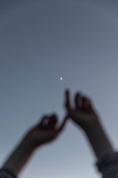 a person holding their hands up in the air with a half moon visible behind them