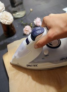 a person is using an iron on top of a piece of paper with flowers in the background