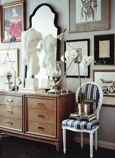 a room with pictures on the wall and a chair in front of a dresser filled with vases