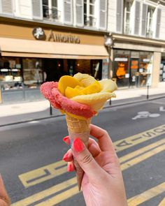 a person holding an ice cream cone with fruit on it in front of a street