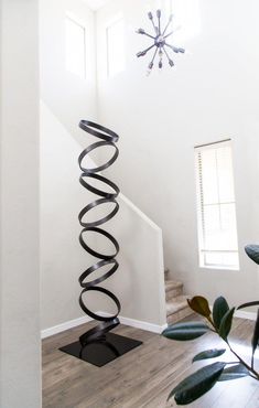 a tall metal spiral sculpture sitting on top of a wooden floor next to a window