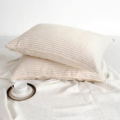 two pillows and a cup sitting on top of a white bed with a striped pillow