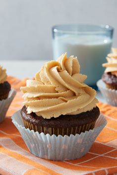 three cupcakes with frosting sitting on an orange and white cloth next to a glass of milk