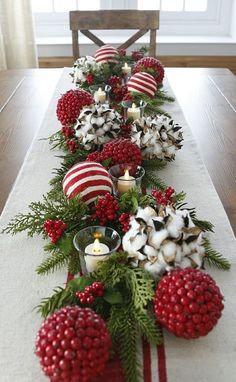 a long table is decorated with red and white balls, greenery, candles and ornaments