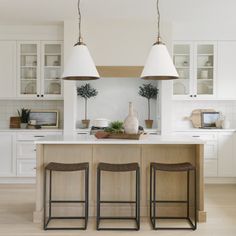 a kitchen with three stools and two lights over the island in front of it