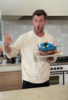 a man holding a cake with candles on it in his hand and giving the thumbs up