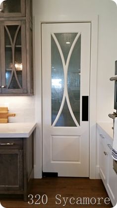 a white door in a kitchen next to a sink and cupboards with glass doors