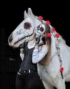 a woman is standing next to a white horse with red roses on it's head