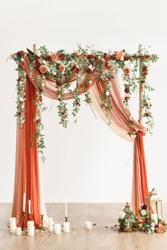 an orange and white wedding arch decorated with flowers, candles and greenery on the floor