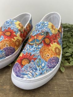 a pair of colorful painted shoes sitting on top of a wooden table next to flowers