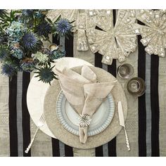 a place setting with silverware and flowers on a striped table cloth, along with napkins