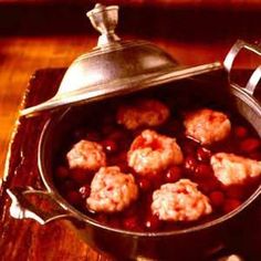 some meatballs and beans in a pot on a wooden table with a teapot