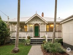 a white house with green door and palm trees in the front yard at sunset or dawn