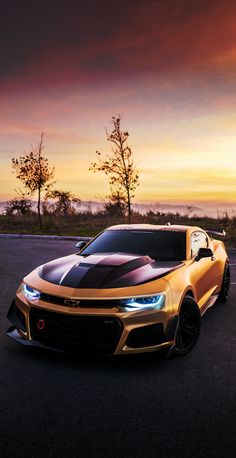 a gold chevrolet camaro is parked on the side of the road in front of an orange sunset