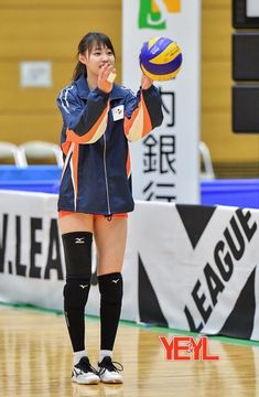 a woman holding a volleyball ball on top of a basketball court in front of a banner