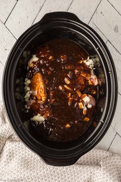 an overhead view of a crock pot filled with chili, chicken and onions on a white table cloth