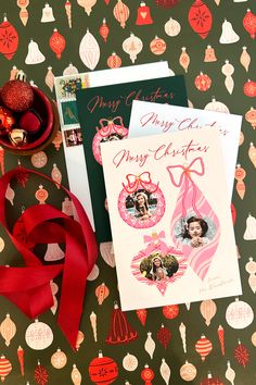 two christmas cards and a red ribbon on top of a table covered in holiday decorations