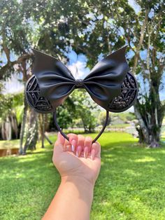 a hand holding up a black bow headband in front of a grassy area with trees