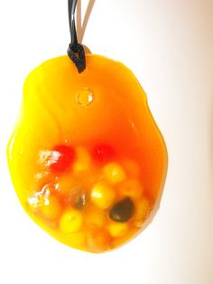 a glass ornament hanging from a black cord on a white background with oranges and yellows in it