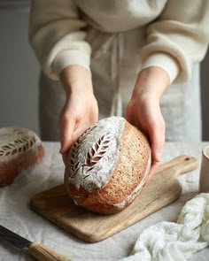 a person holding a loaf of bread on top of a wooden cutting board