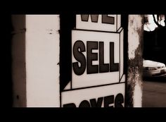 a black and white photo of a sell sign on the side of a building with cars in the background