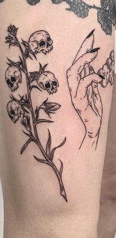 a woman's thigh with skulls and flowers on the side, as well as a hand holding a flower