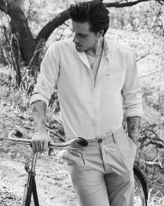 a man with tattoos on his arm standing next to a bike in front of some trees