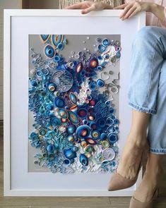 a woman is sitting on the floor holding a framed artwork piece with blue and red designs