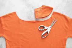 a pair of scissors sitting on top of an orange t - shirt that is cut in half