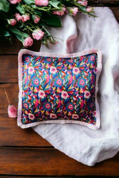 a colorful pillow sitting on top of a wooden table next to pink and green flowers