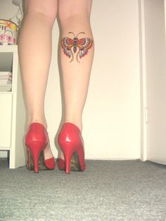 a woman's legs with tattoos on them and red shoes in front of a white wall