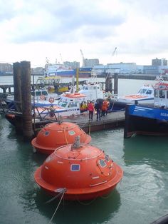 two orange buoys sitting in the water next to a dock with people standing on it