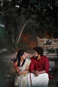 a man and woman sitting next to each other in front of a tree with leaves